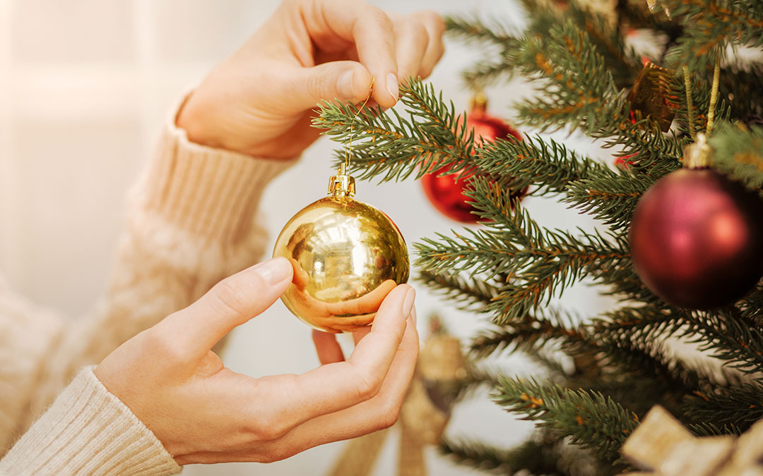 Person decorating a christmas tree with a gold bauble 