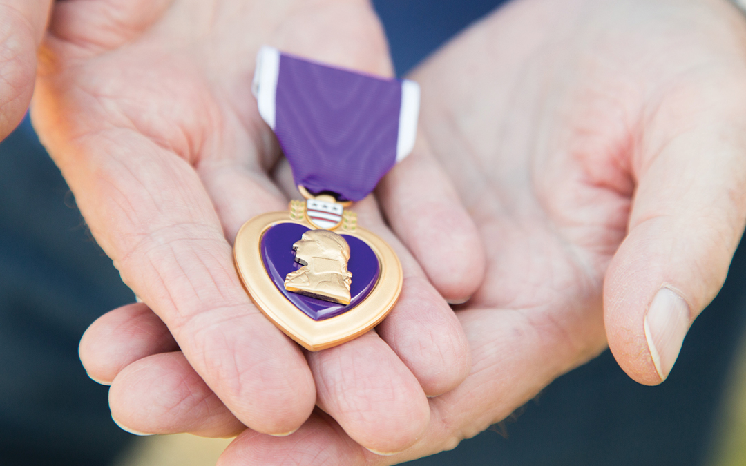 Hands holding a Purple Heart badge in honor of Purple Heart Day.